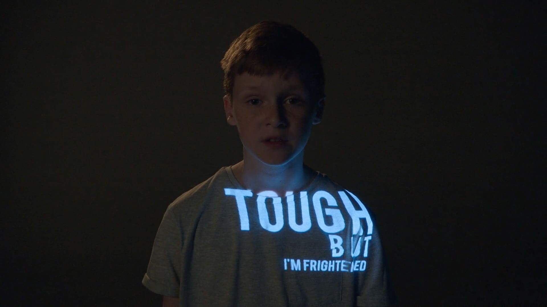 Young boy with the words TOUGH BUT I'M FRIGHTENED projected onto his t-shirt